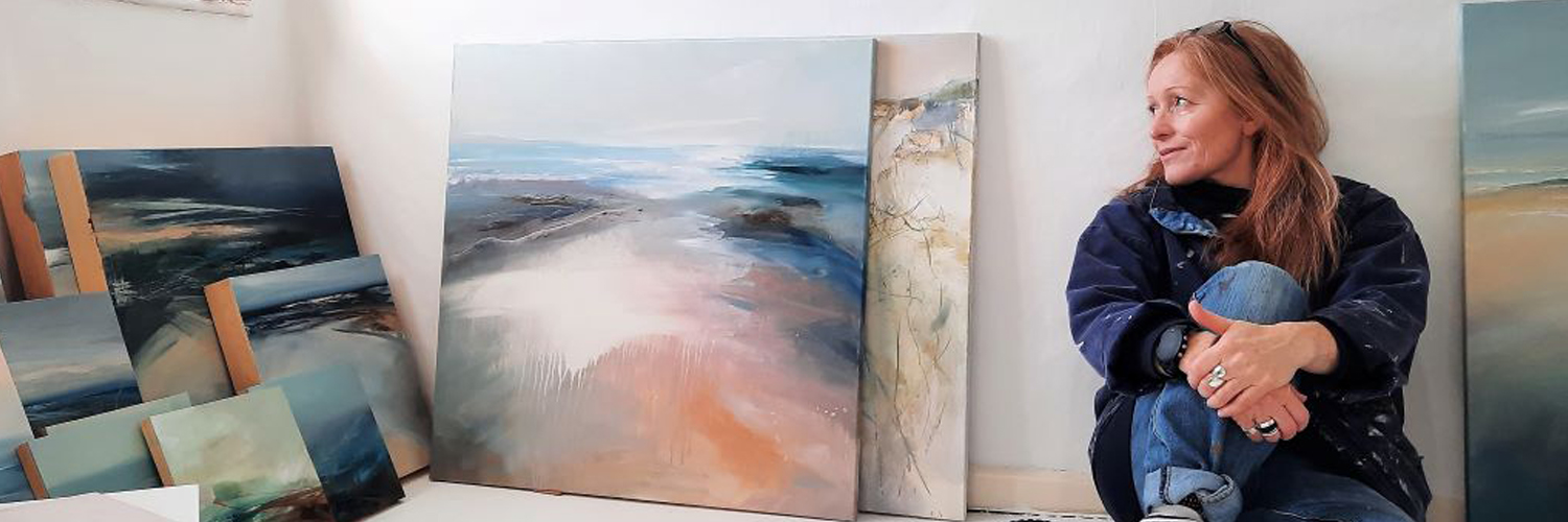 Photo of the artist, Angela Sowden, sitting in her studio with her paintings. Contemporary landscape art.